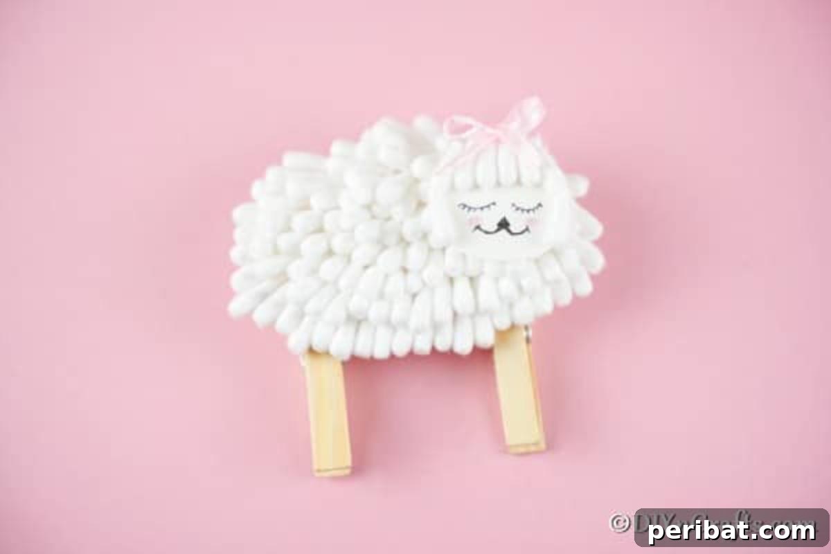 Completed lamb craft displayed on pink paper, highlighting its fluffy cotton swab texture and clothespin legs.