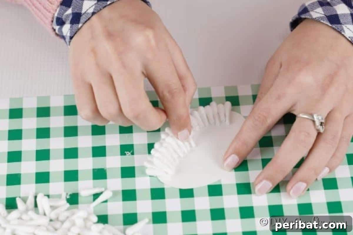 Applying craft glue and meticulously placing cotton swab halves onto the oval body, creating a fluffy and textured lamb body.