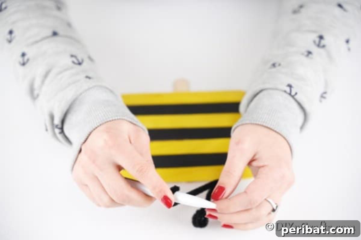 A black pipe cleaner being wrapped around a pen to create a curled antenna for the craft stick bee.