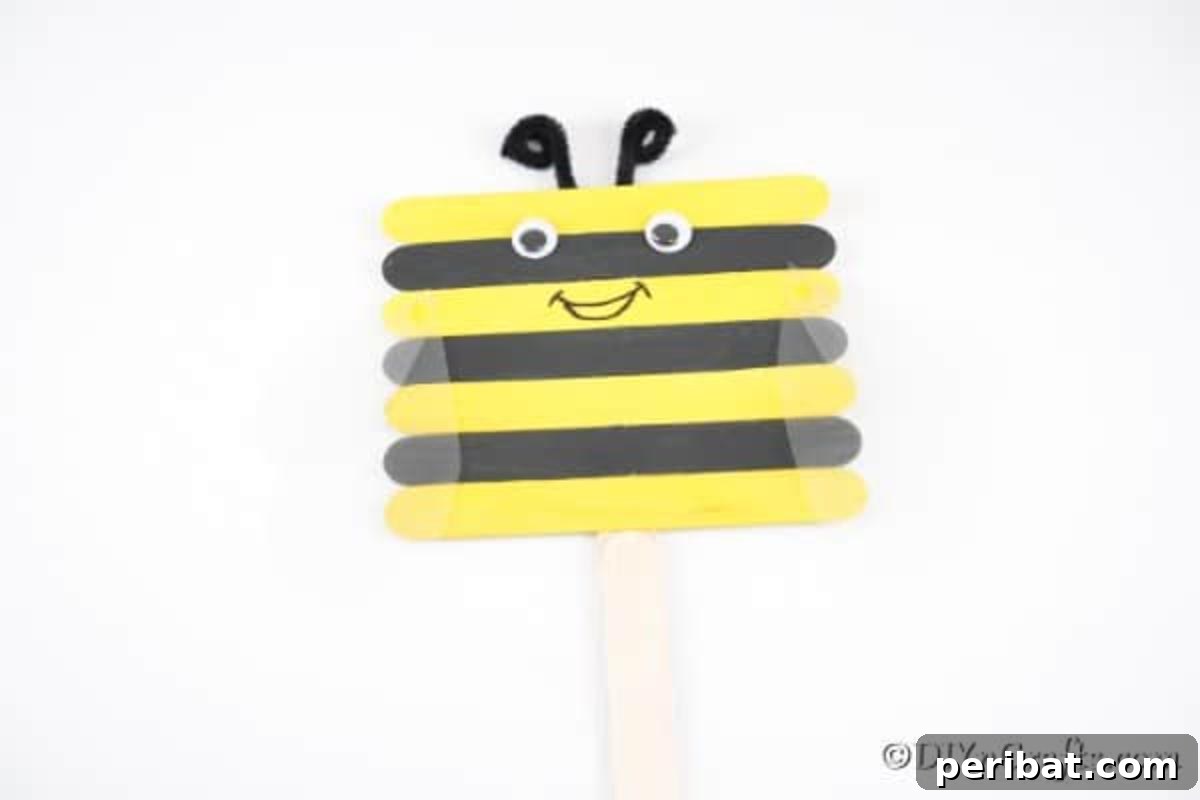 A finished craft stick bee positioned on a clean white surface, showcasing its cheerful design and details.