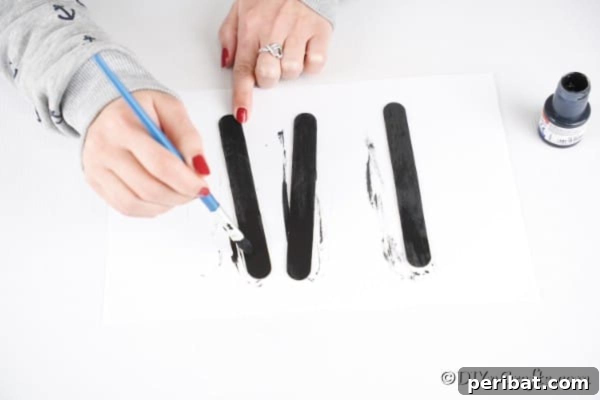 Craft sticks being painted black on a protected surface, illustrating the first step of the project.