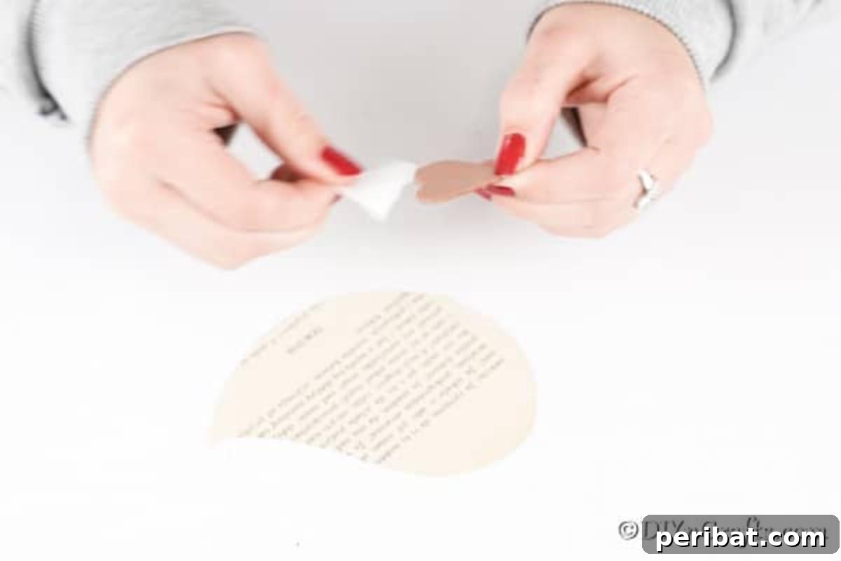 DIY Vintage Book Page Bird Wall Art 13 A hand carefully attaching a glittery heart cutout, positioned upside down, to the body of a book page bird, creating its wings.