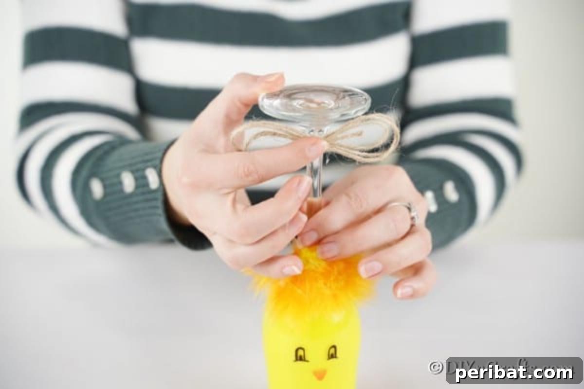 Adorable DIY Chick Wine Glass Luminary 12 A close-up view of hands tying a rustic jute bow onto the stem of a painted wine glass, adding a finishing touch.
