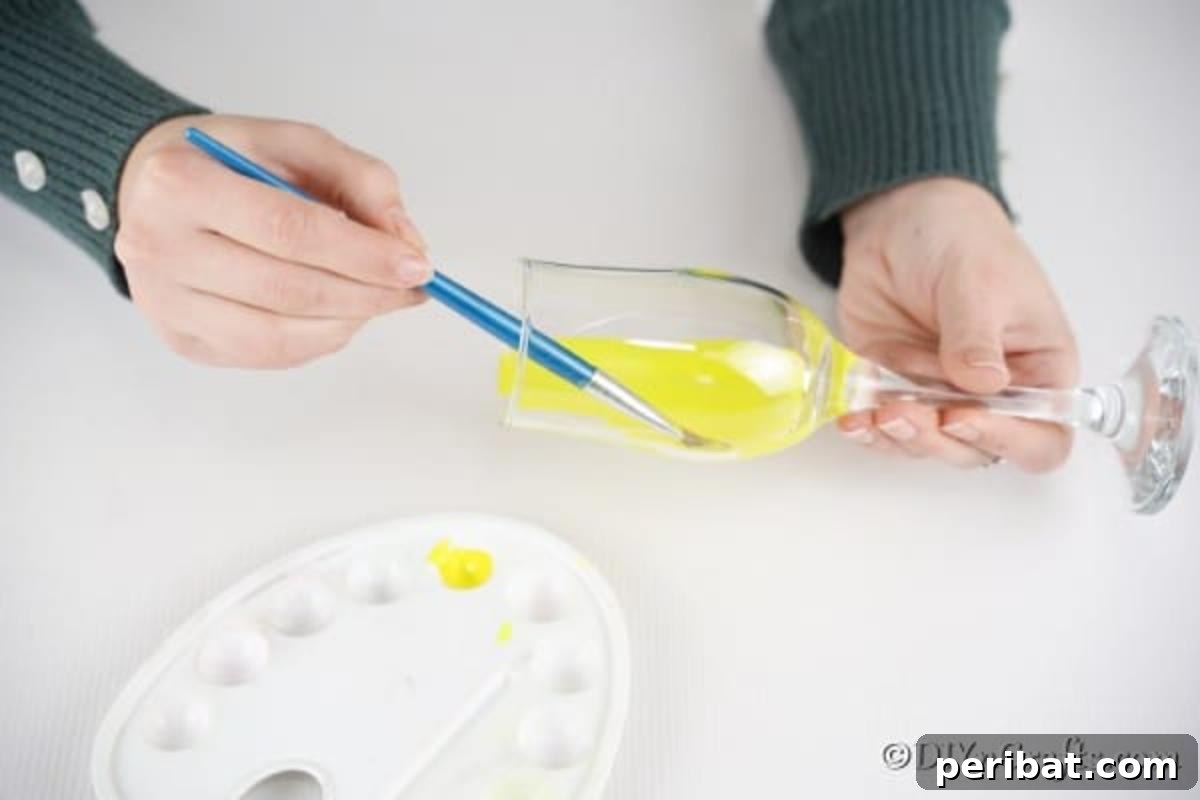Adorable DIY Chick Wine Glass Luminary 9 A hand carefully paints the inside of a wine glass with yellow paint, beginning the transformation into a charming candle holder.