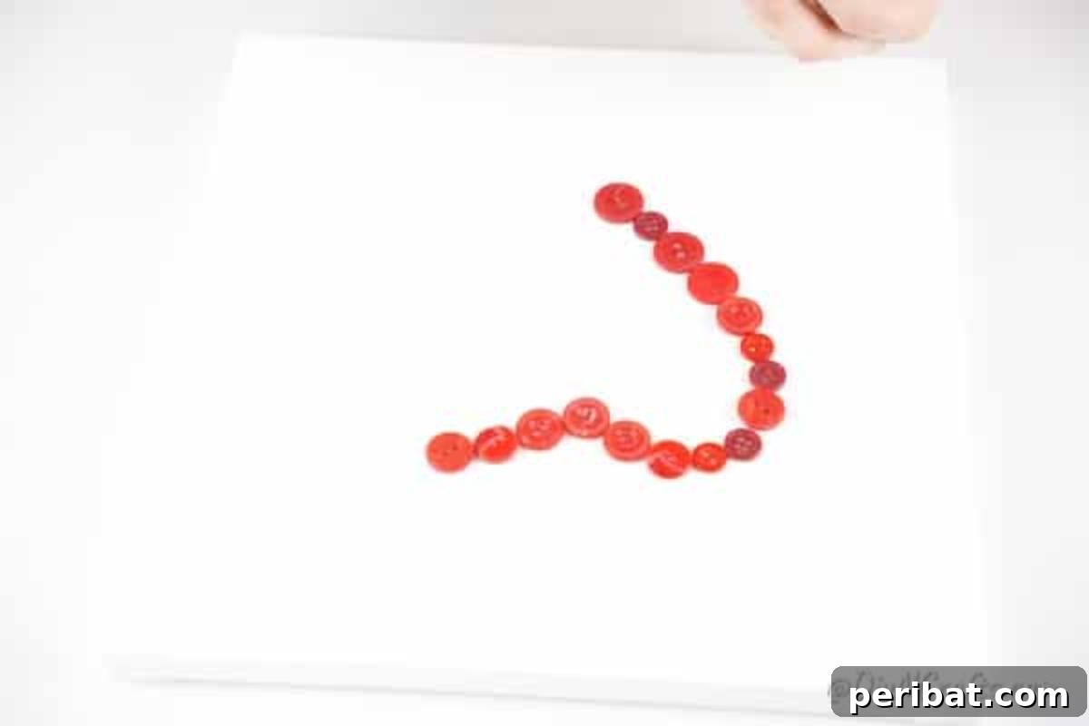 Charming Button Heart Canvas Decor 10 A close-up of hands carefully gluing red buttons along the pencil outline of a heart on a canvas.