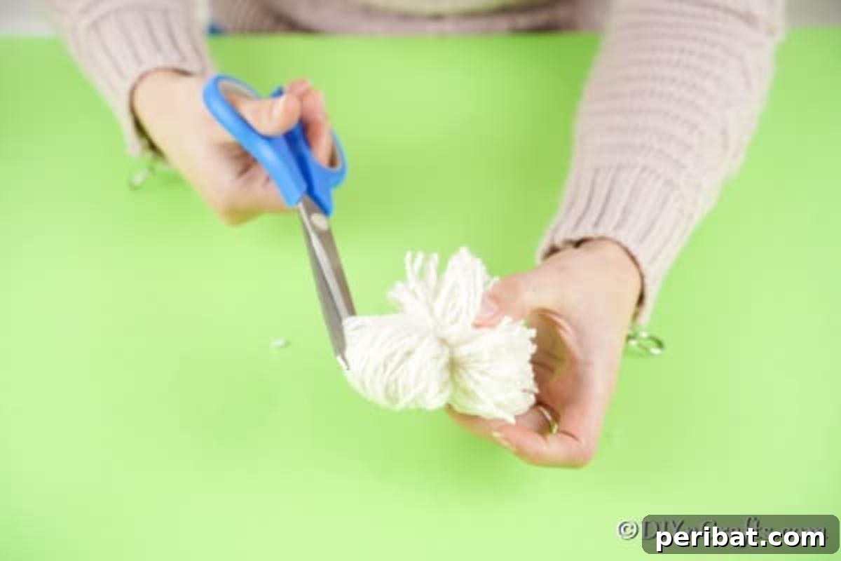 Fluffy Pom-Pom Sheep: A DIY Video Craft Guide 10 A close-up of scissors cutting through the loops of yarn on one side of a tied pom pom, preparing it to be fluffed into its final spherical shape.