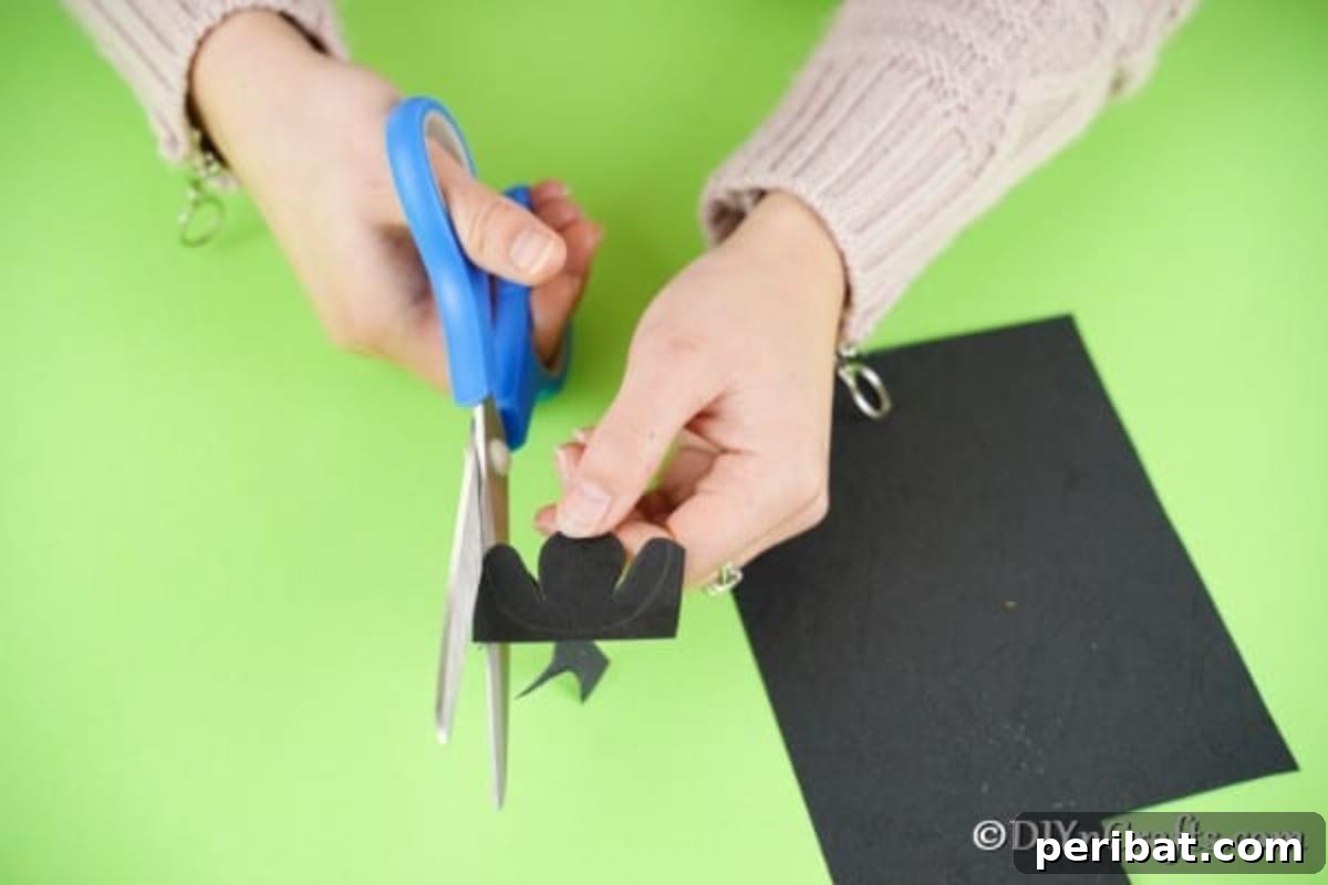Fluffy Pom-Pom Sheep: A DIY Video Craft Guide 12 A hand holding black craft paper with a drawn sheep face outline, while another hand uses scissors to carefully cut out the shape, preparing the facial features for the pom pom sheep.