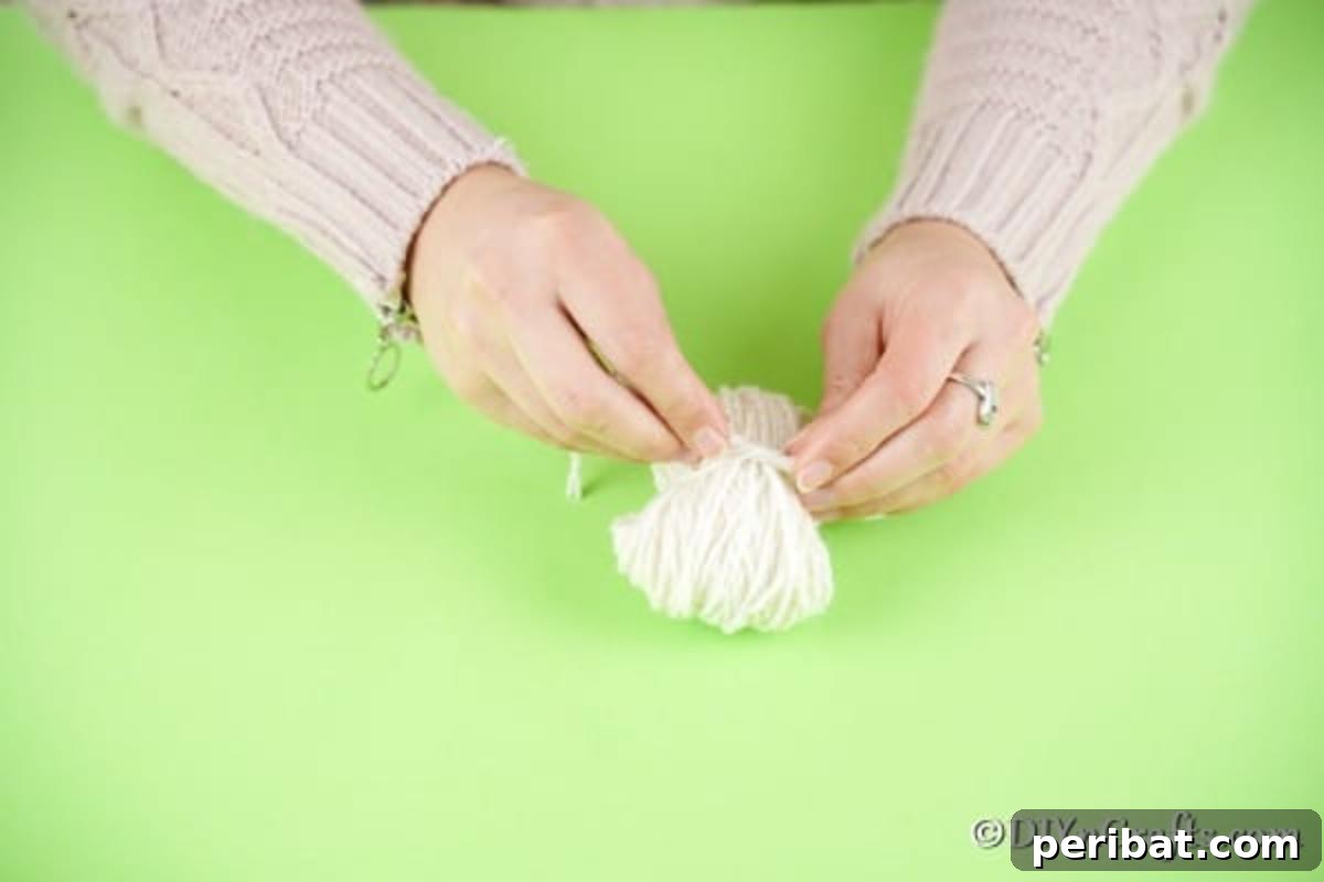 Fluffy Pom-Pom Sheep: A DIY Video Craft Guide 9 Hands carefully tying a short piece of yarn around the pinched center of a wrapped yarn bundle, securing the initial form of a pom pom.