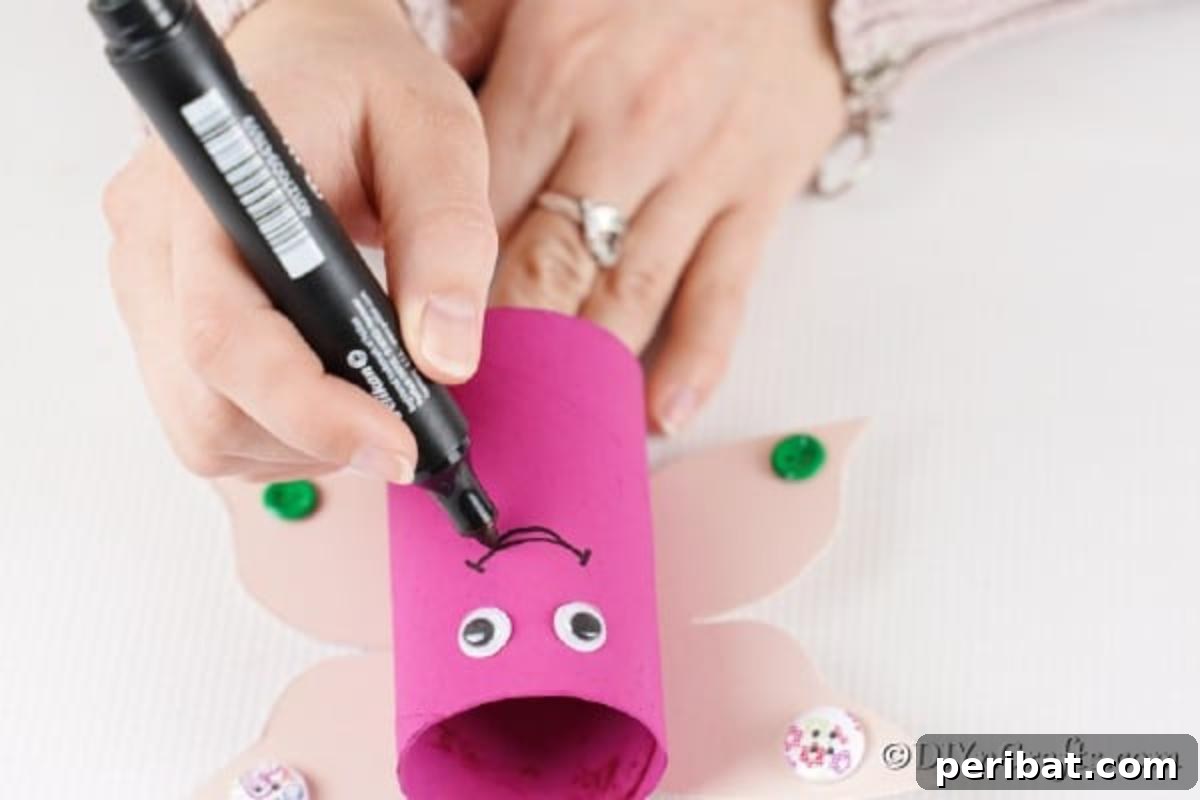 Drawing a smile on a painted toilet paper roll with googly eyes for a butterfly craft