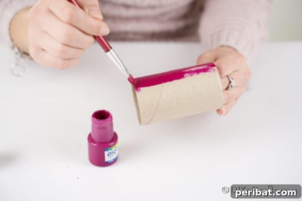 Child's hand painting a toilet paper roll pink