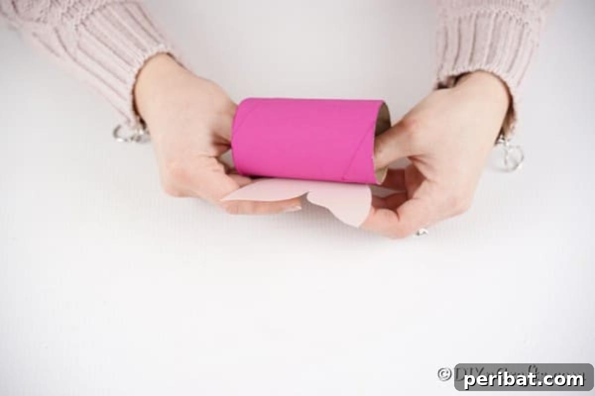 Craft glue being applied to attach paper wings to a pink toilet paper roll