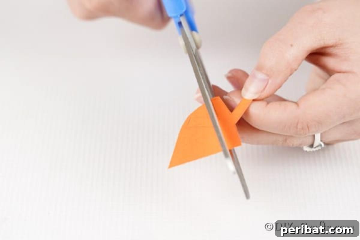 Colorful Craft Stick Chicken Painting 14 A small orange triangle being cut from craft paper to form the beak of the popsicle stick chick.