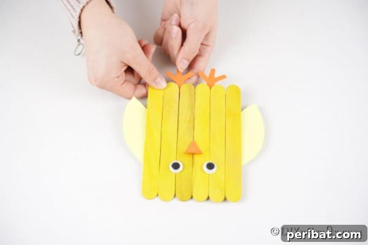 Colorful Craft Stick Chicken Painting 15 Orange paper beak and feet being carefully glued onto the yellow popsicle stick chick.