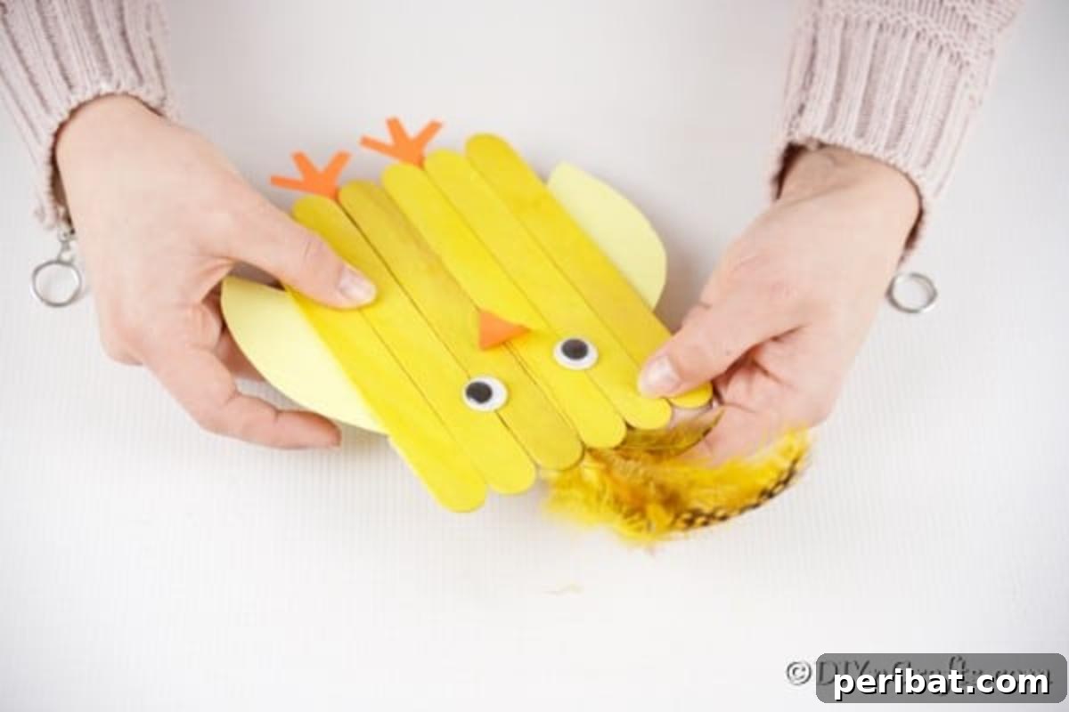Colorful Craft Stick Chicken Painting 16 A small yellow feather being glued to the back of the craft stick chick's head for a fluffy look.