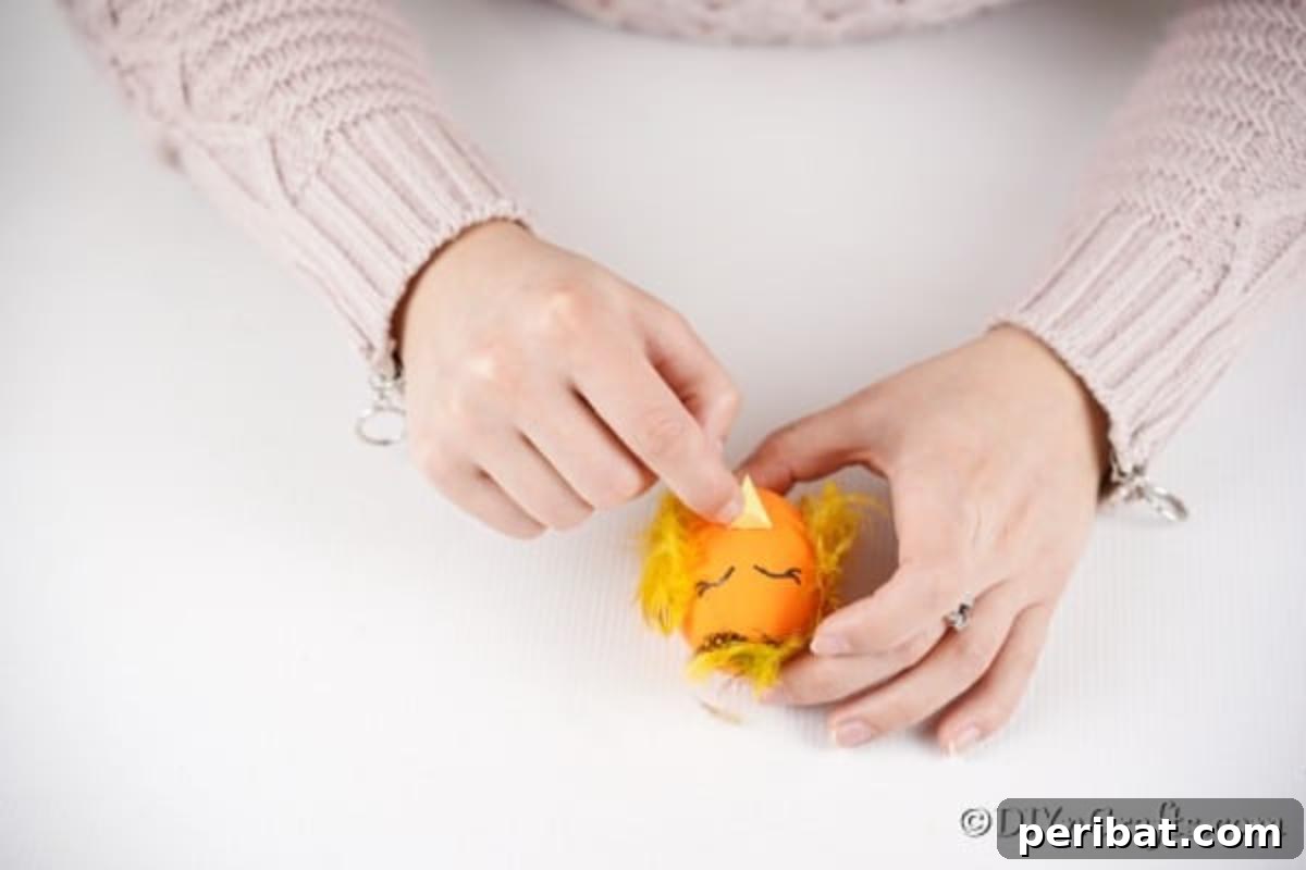 Craft Adorable Easter Egg Chickens A Step by Step Video Guide 12 The final step of gluing the yellow paper beak onto the egg, completing the chick's face
