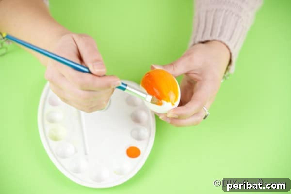 Craft Adorable Easter Egg Chickens A Step by Step Video Guide 8 A close-up shot of an egg being painted orange with a paintbrush, demonstrating the first step of the craft