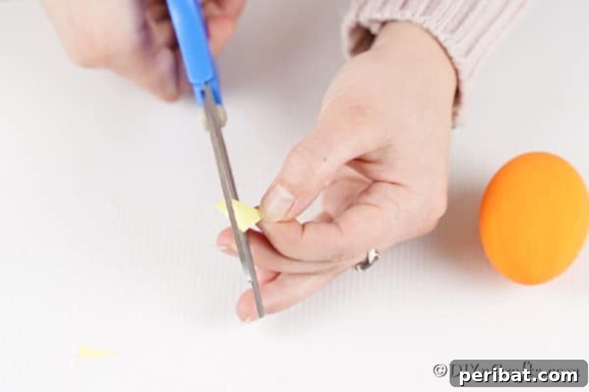 Craft Adorable Easter Egg Chickens A Step by Step Video Guide 9 A hand demonstrating how to cut a small diamond shape from yellow craft paper to form the chicken's beak