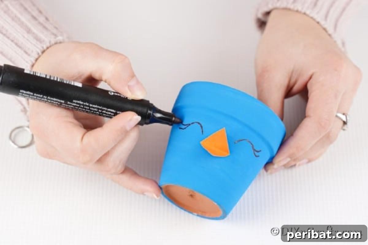 Whimsical Hand-Painted Bird Planter Charm 10 Drawing eyes onto the blue bird flower pot with a black paint pen