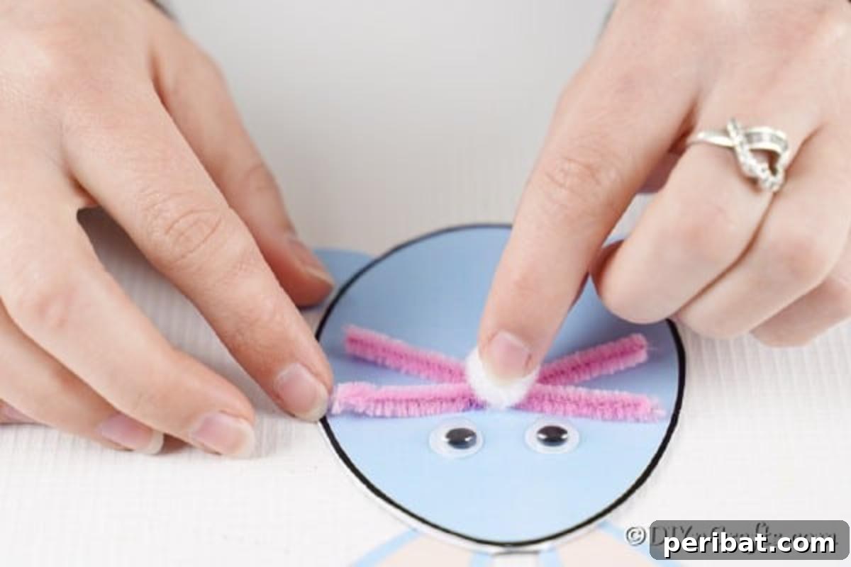 Hands meticulously gluing pipe cleaners as whiskers and a white pom-pom as the nose to the bunny's face.