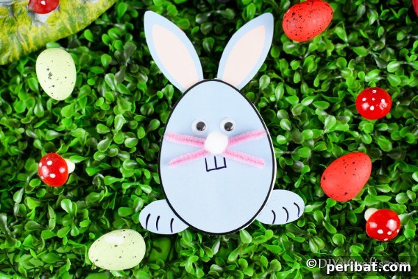 A finished egg-shaped Easter bunny card resting on a green, textured surface, ready for gifting or display.