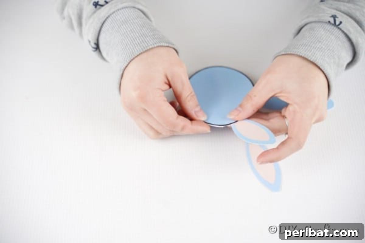 Hands gluing the two ear shapes onto the top fold of the egg-shaped card, showing how to position them.