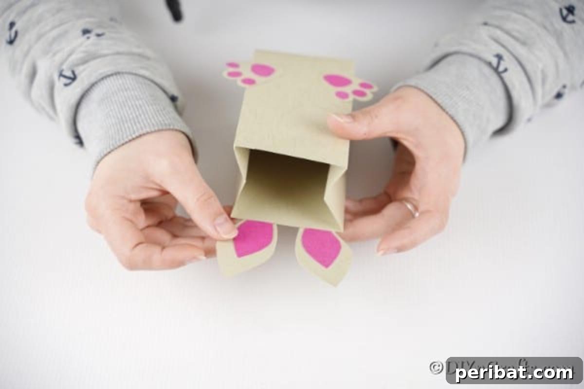 DIY Easter Treat Pouch Video Guide 17 Hands gluing the completed bunny ears to the top back of the paper bag