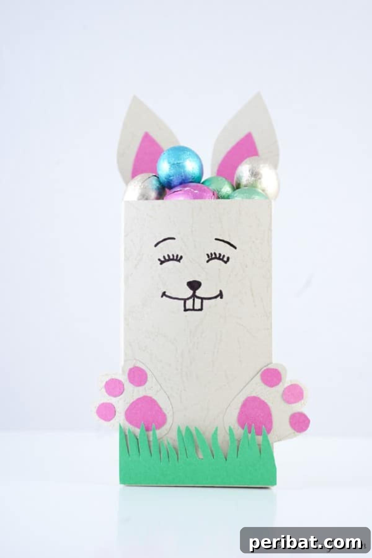 DIY Easter Treat Pouch Video Guide 5 Close-up of a finished paper bag Easter candy holder with bunny ears and feet, sitting on a white surface