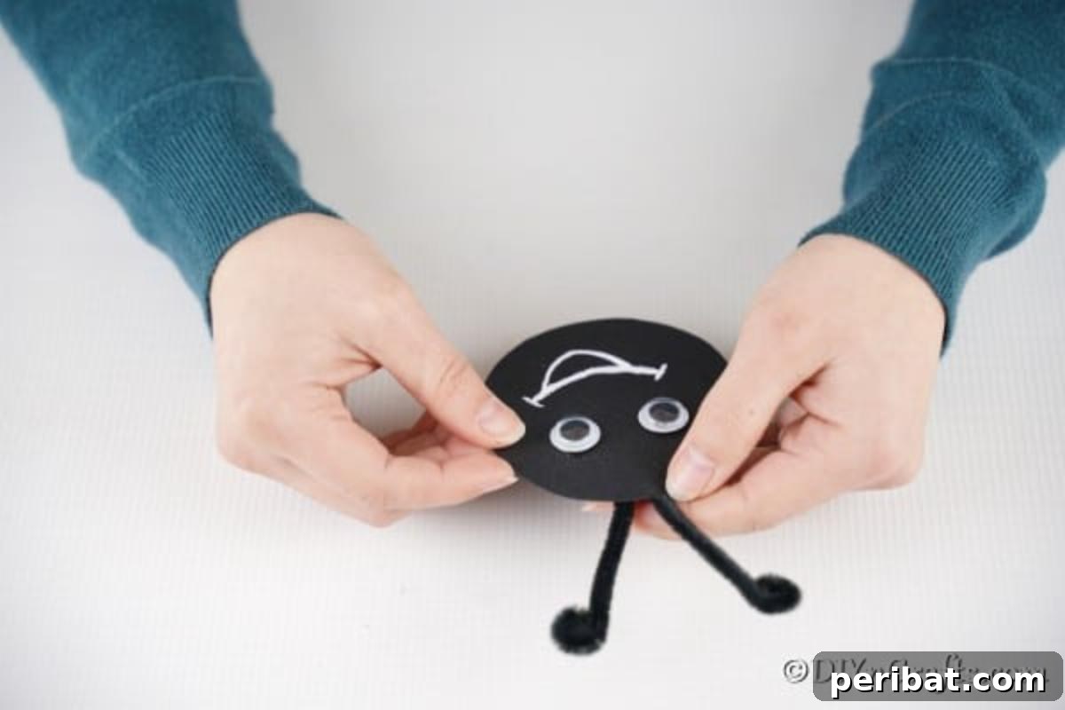 Repurposed Ladybug Bowl Art 11 Curled black pipe cleaners being attached to the back of the ladybug's paper face, forming the antennae.