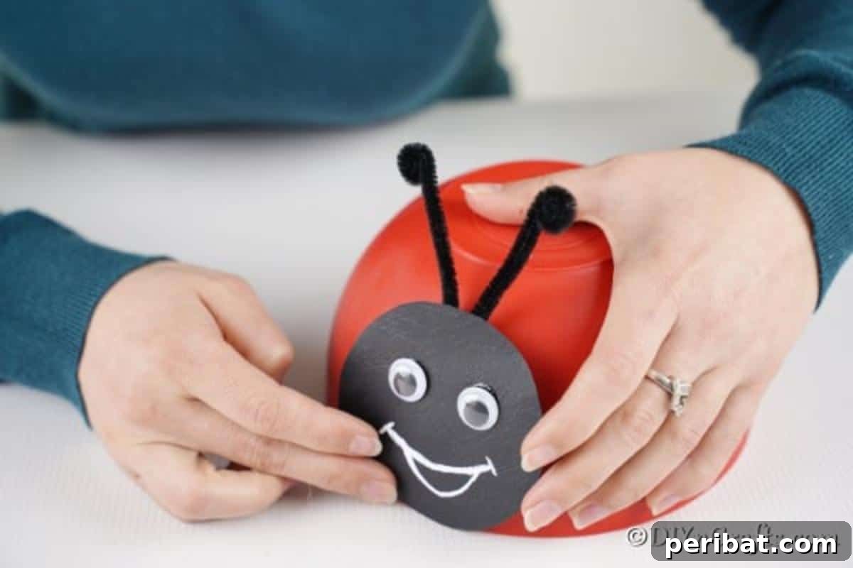 Repurposed Ladybug Bowl Art 12 A person gluing the completed ladybug face onto the side of a red plastic bowl, attaching the head to the body.