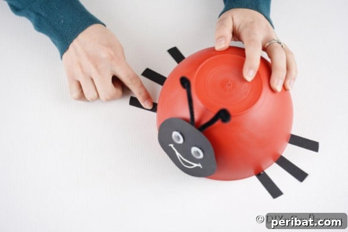 Repurposed Ladybug Bowl Art 13 A person gluing black paper strips onto the underside of the red bowl, creating the ladybug's legs.