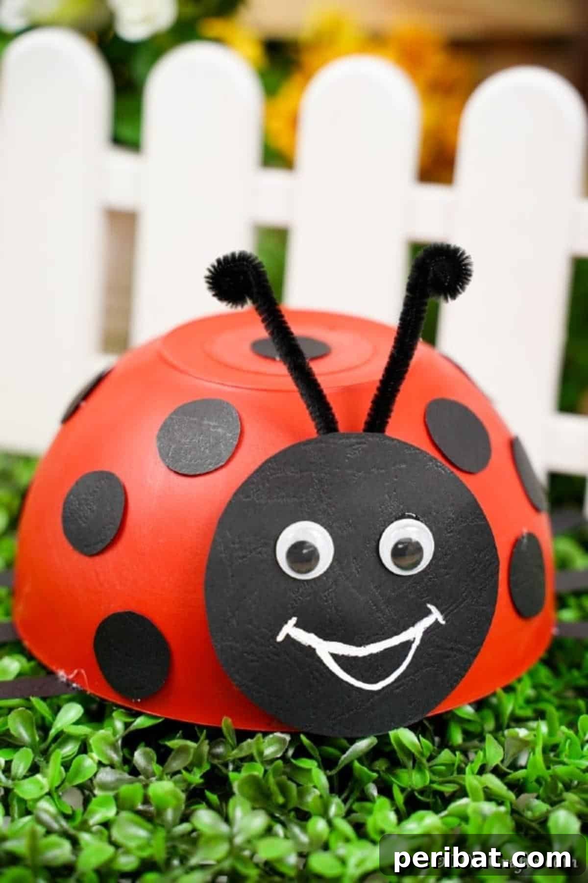 Repurposed Ladybug Bowl Art 3 Handcrafted red bowl ladybug decoration placed in front of a quaint white picket fence, symbolizing a charming garden accent.