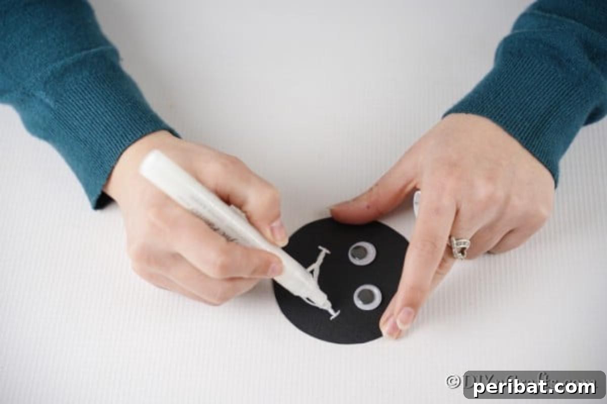 Repurposed Ladybug Bowl Art 10 A black paper circle with googly eyes and a hand drawing a white smile with a paint pen, forming the ladybug's face.