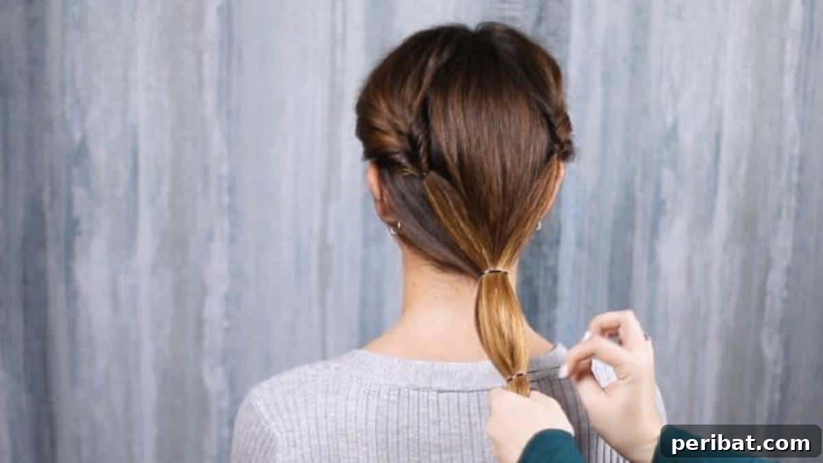 Rose-Kissed Low Bun Updo 14 Securing the low ponytail halfway down its length with a second rubber band, a crucial step for the bun's structure.