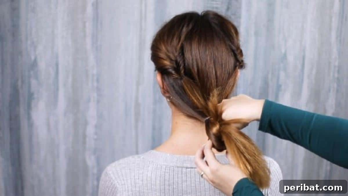 Rose-Kissed Low Bun Updo 15 The lower part of the ponytail being pulled through an inversion, creating a beautiful twist and preparing for the bun.