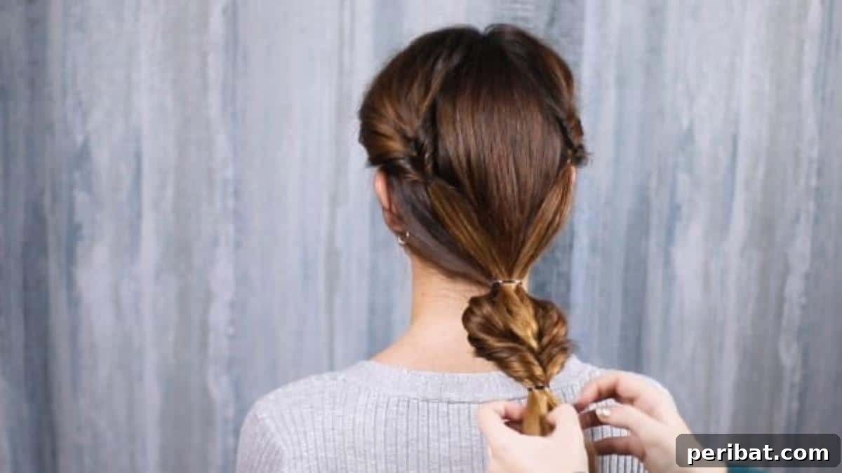 Rose-Kissed Low Bun Updo 16 Hands gently loosening and fluffing the hair between the two ponytail holders to achieve a softer, more voluminous style.