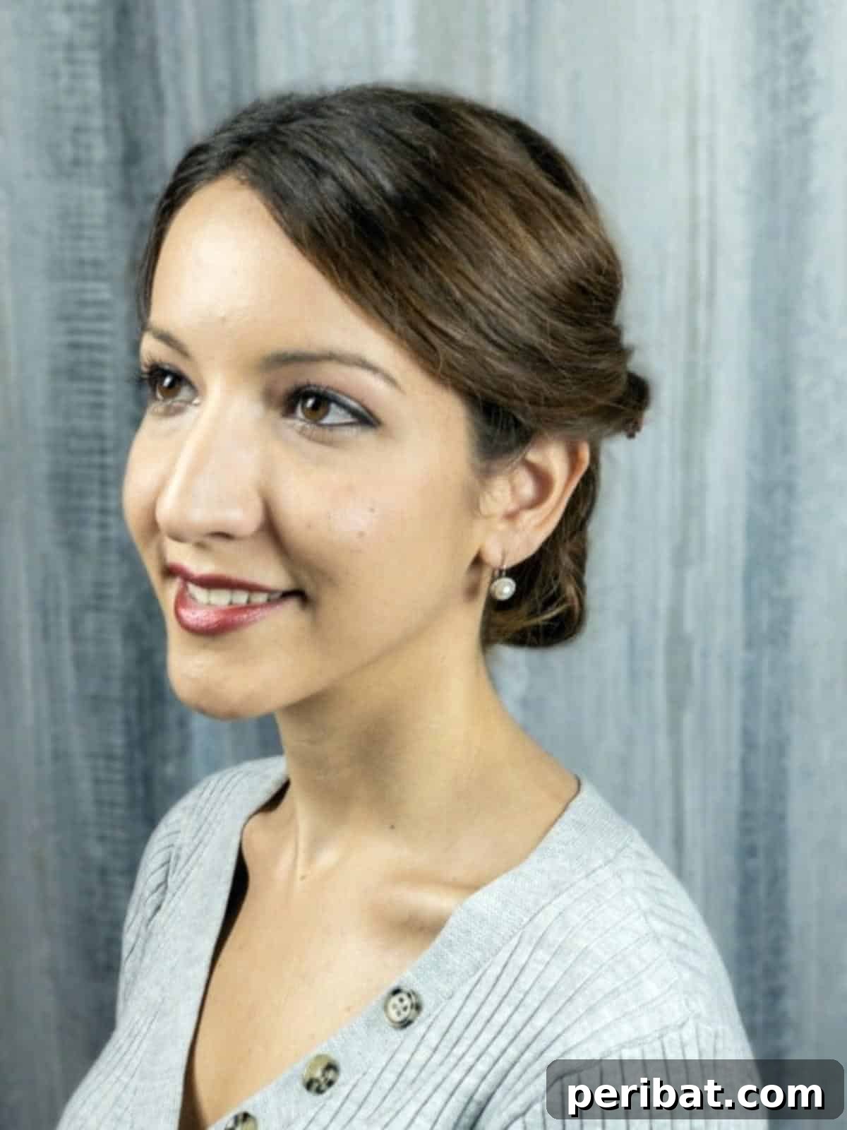 Rose-Kissed Low Bun Updo 3 A woman with beautiful brunette hair showcasing the low bun updo with a soft, elegant twist, wearing a stylish grey top.