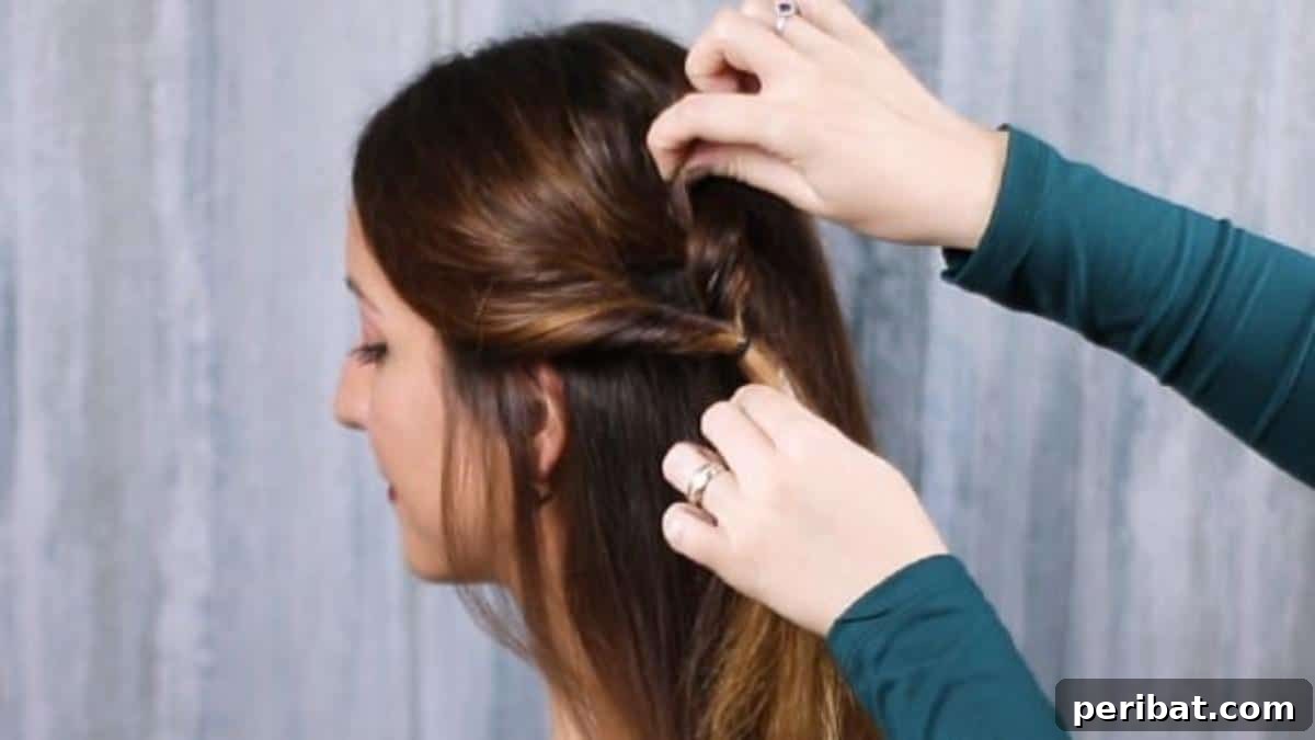 Rose-Kissed Low Bun Updo 10 Hands gently pulling and fluffing the twisted hair section to create a softer, more voluminous look around the face.