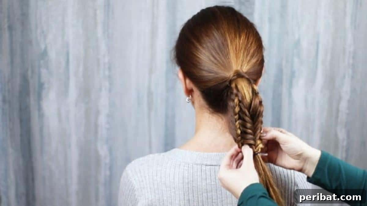 The finished fishtail ponytail being tied in place, showing the gentle pulling for volume