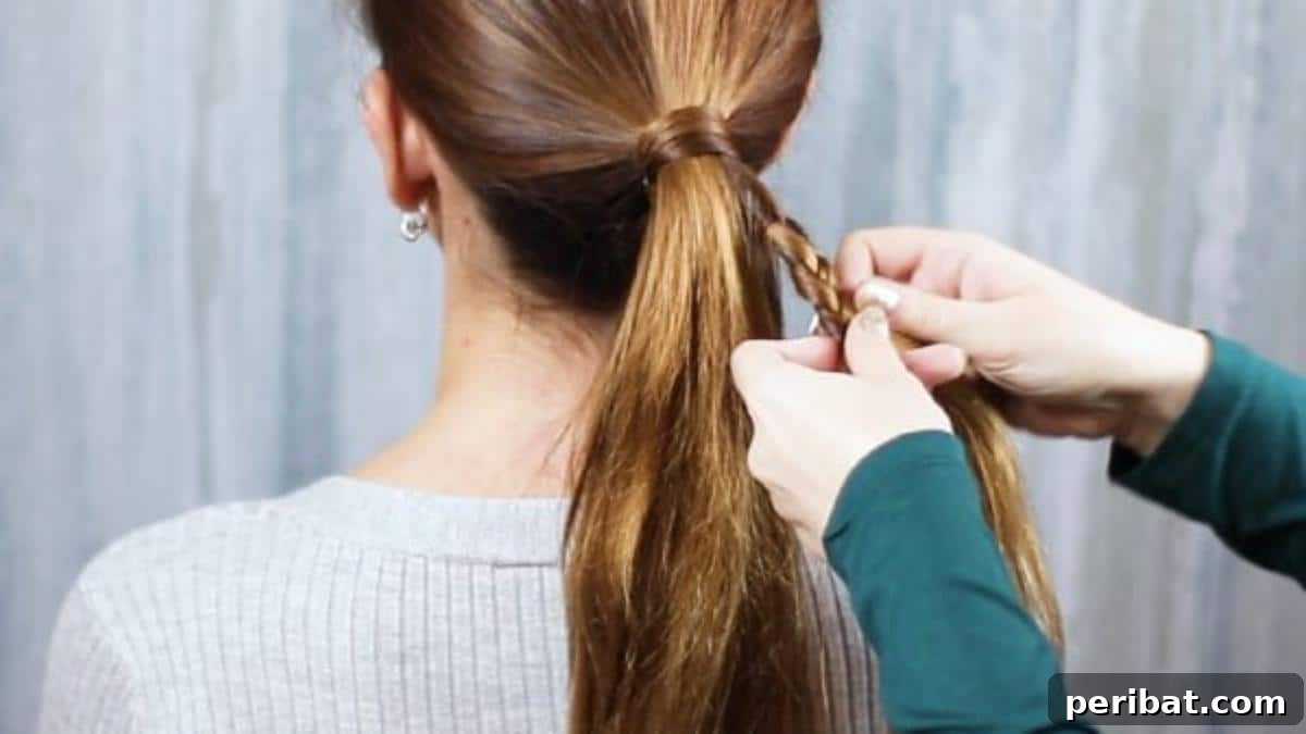 Hands braiding a small piece of hair taken from one side of the ponytail