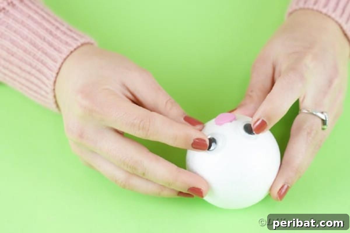 DIY Adorable Easter Bunny Wreath Video Guide 12 Attaching googly eyes and a pink paper nose to the styrofoam ball for the bunny's face.