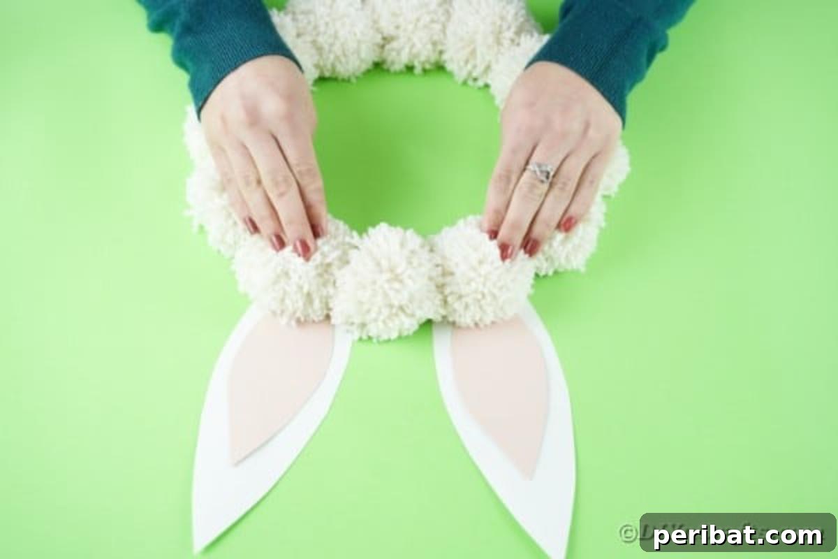 Fluffy Pom Pom Easter Bunny Door Wreath 16 Attaching the assembled bunny ears to the back of the cardboard wreath frame.