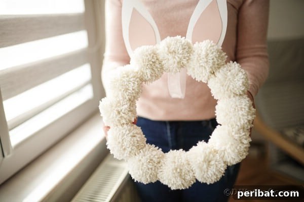 Fluffy Pom Pom Easter Bunny Door Wreath 19 A person holding a beautifully crafted DIY Pom Pom Easter Bunny Wreath.
