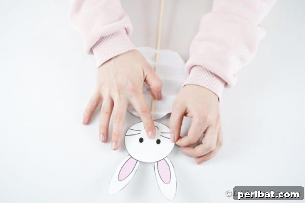 DIY Easter Paper Bunny Craft Free Printable Template 14 Image showing the bunny head being glued onto the top of the dowel rod