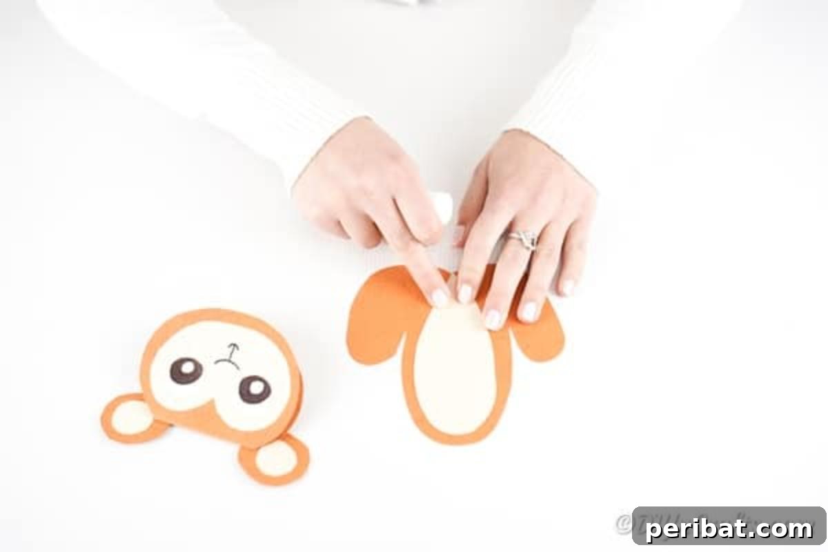 DIY Monkey Card Fun for Kids 16 A cream oval piece is being glued onto the center of the orange paper monkey body, forming the distinct belly detail.