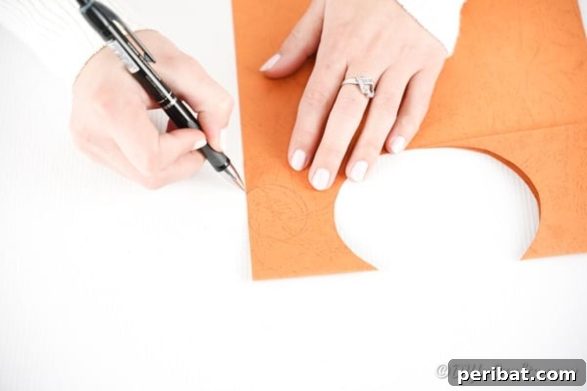 DIY Monkey Card Fun for Kids 9 A hand drawing two small, rounded ear shapes onto a piece of orange craft paper, preparing them for cutting and assembly.