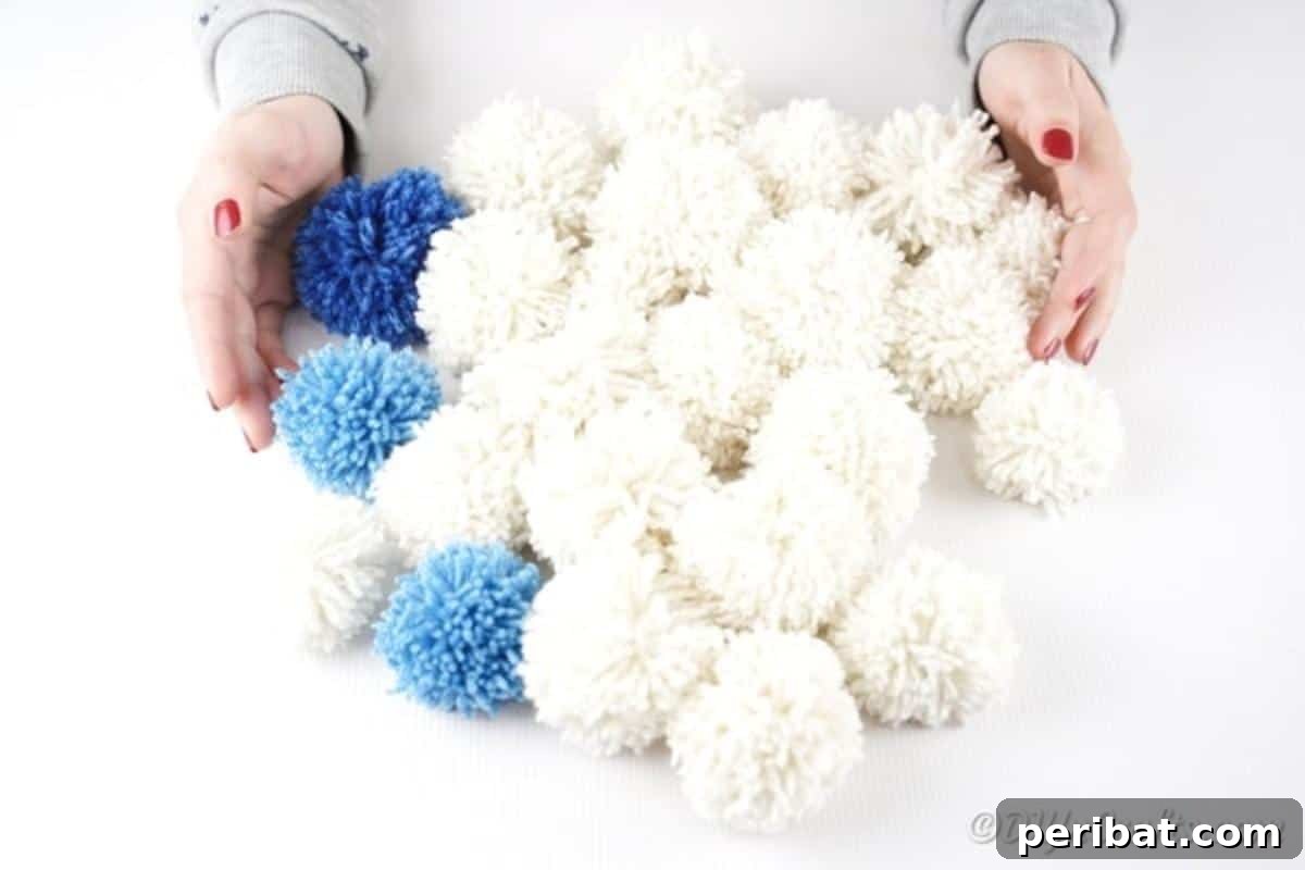 Several finished yarn pom poms in white, dark blue, and light blue
