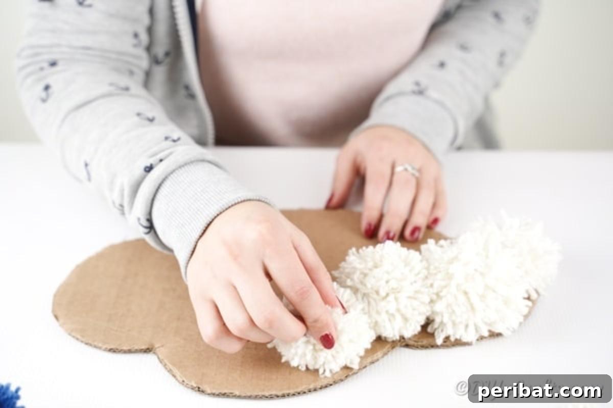 Gluing white yarn pom poms onto the cardboard cloud base