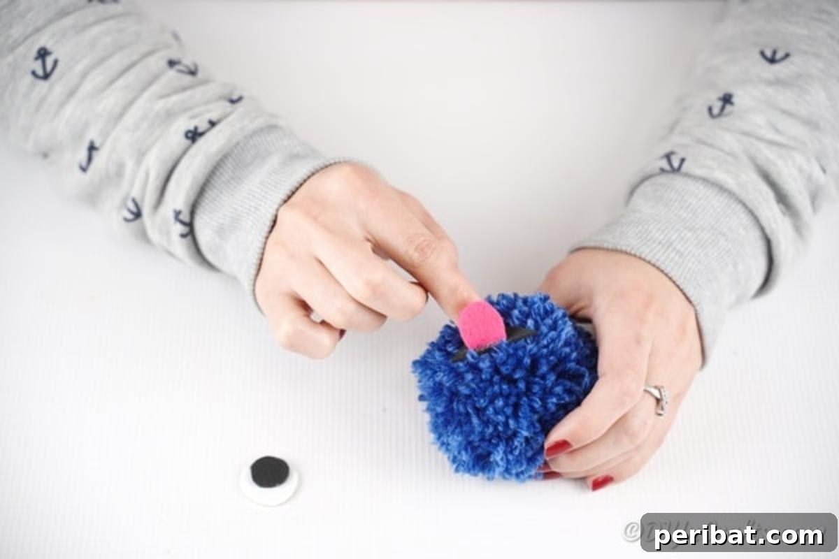 Pink paper tongue being glued onto a blue yarn pom pom