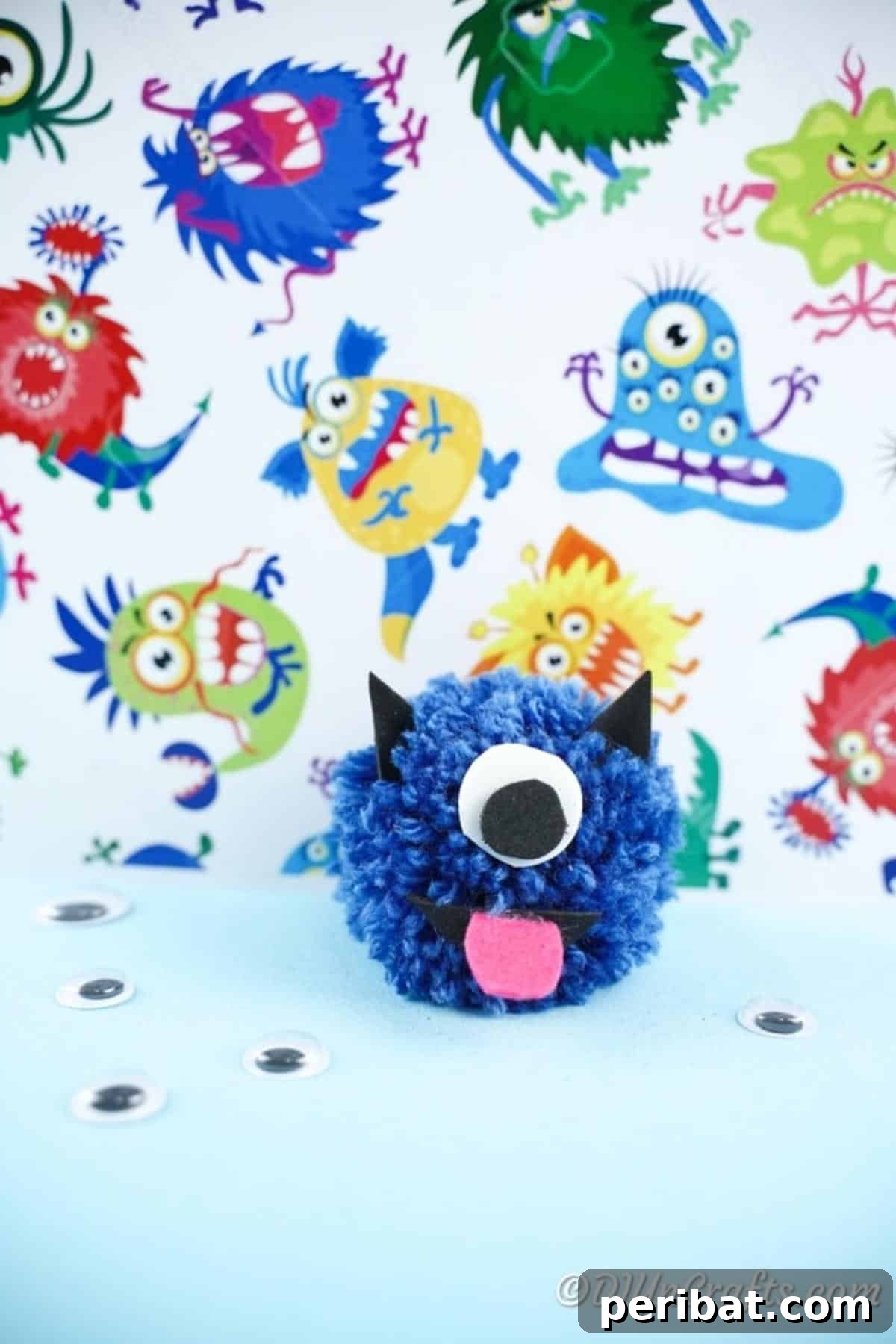 Cute blue yarn pom pom monster in front of monster-themed patterned paper