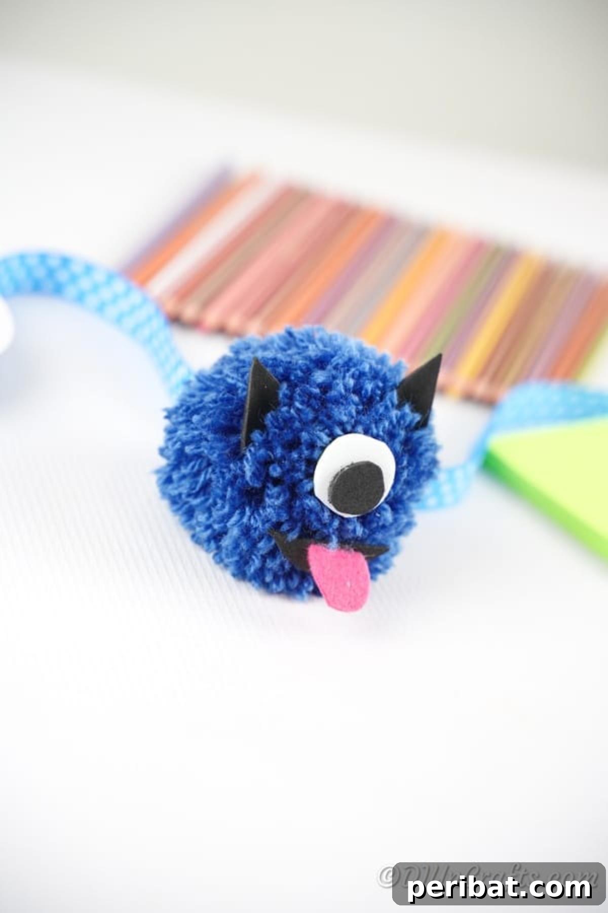 Finished pom pom monster with craft supplies like colored pencils and paper